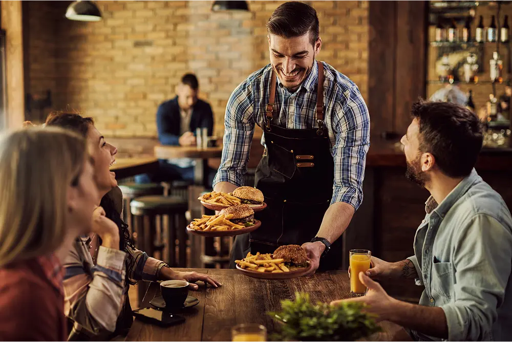 Happy waiter serving food to a group of cheerful friends in a pub