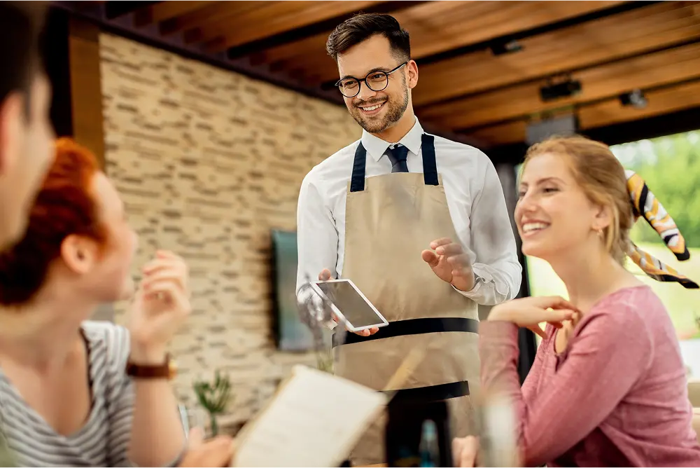 Young happy waiter taking order from his guests in a cafe