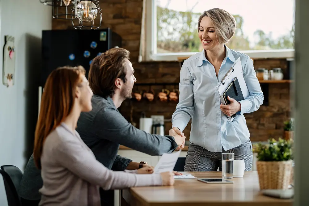 happy insurance agent meeting with young couple shaking hands with man their home