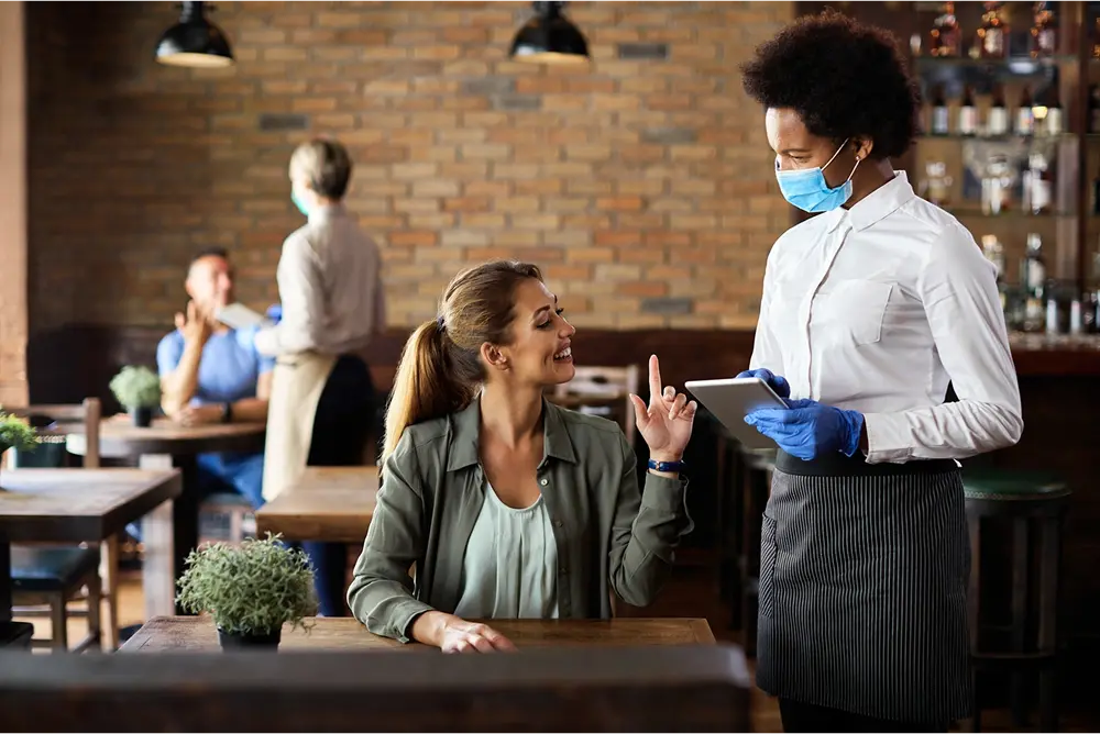 Happy woman making order while talking to black waitress at cafe.