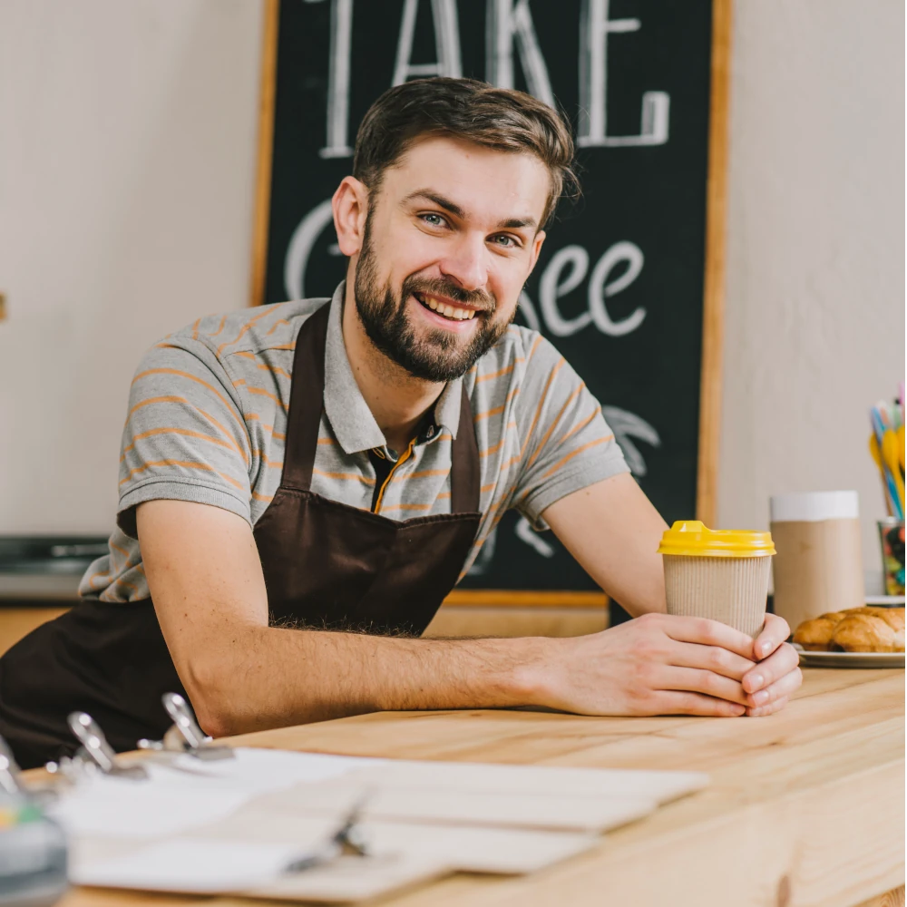 A male barista smiles at the camera while making a coffee